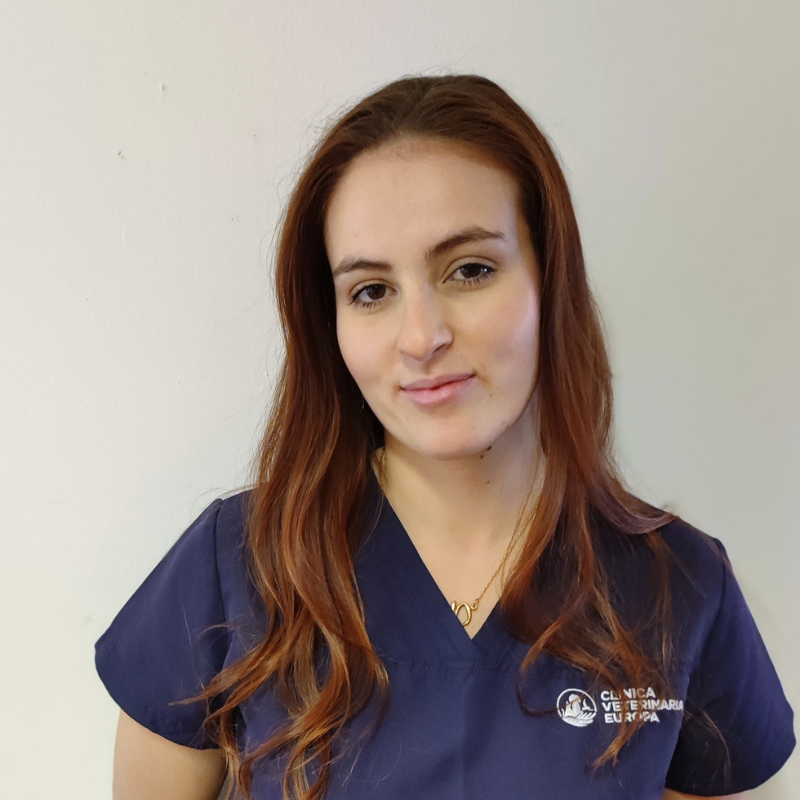 Una donna dai lunghi capelli ramati che indossa un camice da medico blu navy si staglia su un semplice sfondo chiaro, guardando la telecamera con un leggero sorriso.